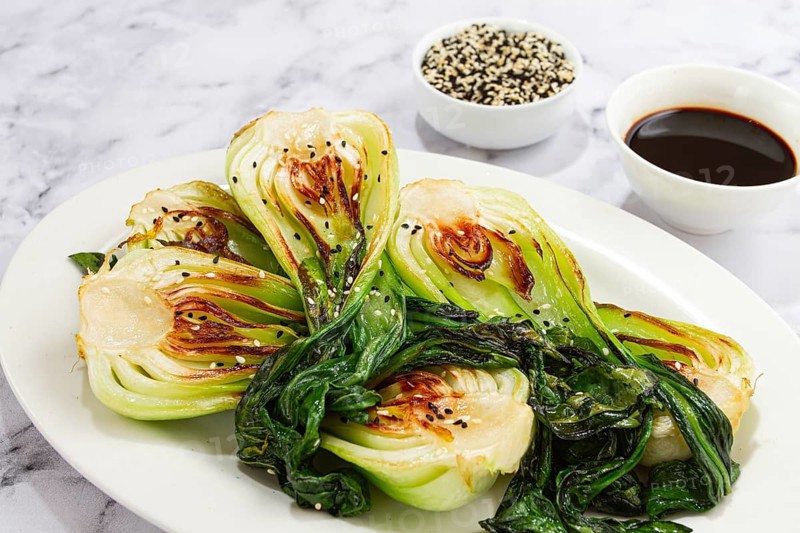 Grilled bok choy served with soy sauce and sesame seeds, on a white plate, homemade, no people