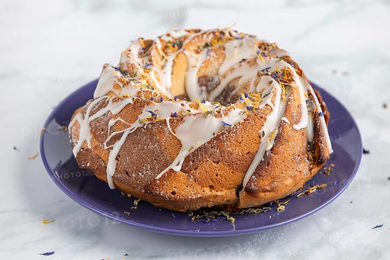 Marble bundt cake, cake with icing and edible flowers on a blue plate, light background
