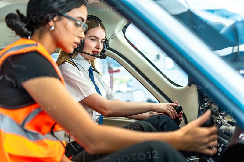 Female pilot and engineer working together inside the cockpit of a small airplane, preparing for take off