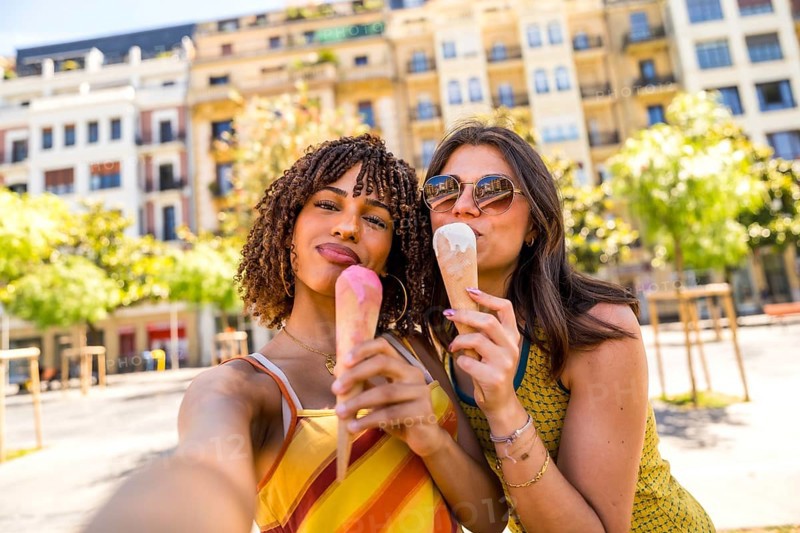 Two friends savoring ice cream cones on a sunny day in a vibrant city square, showcasing joy and friendship in an urban environment