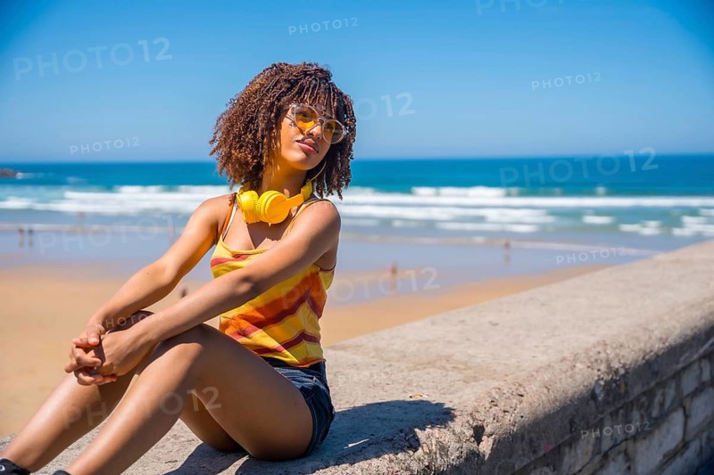 Young woman soaking up the summer sun and ocean breeze, enjoying music through her headphones while relaxing on the beach