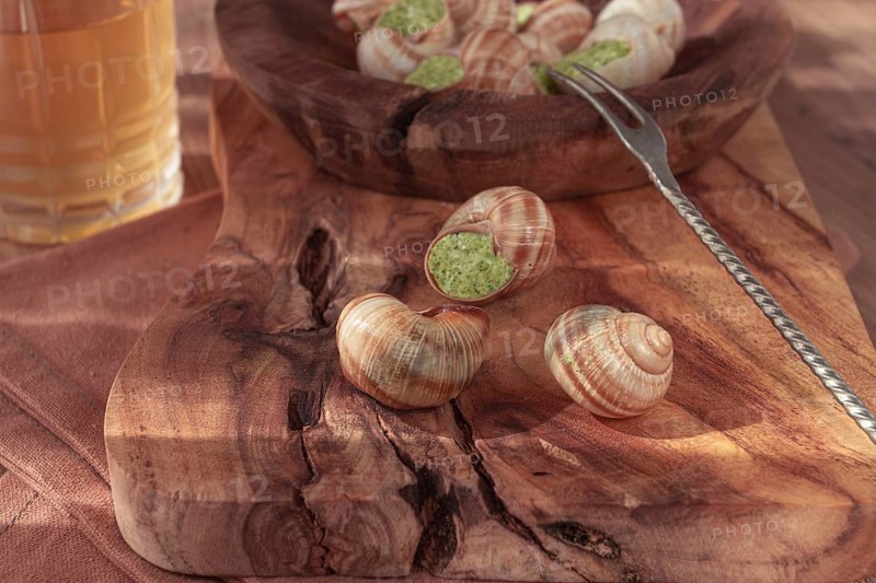 Snails cooked with herb oil on a wooden plate, served with white wine, natural light, no people