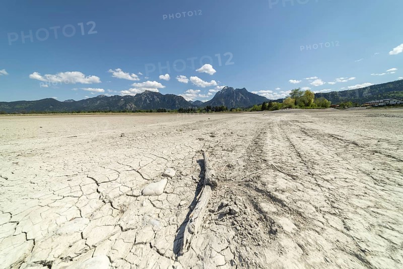 Cracked, dried out ground, waterless Forggensee in spring, behind it Tegelberg massif and Säuling, Ammergau Alps, near Füssen, Ostallgäu, Bavaria, Germany, Europe