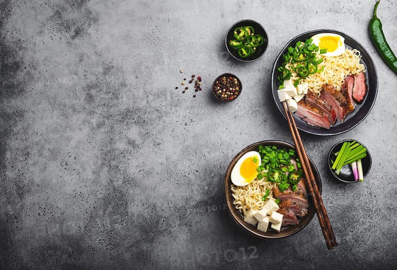 Two bowls of tasty Asian noodle soup ramen with broth, tofu, pork, egg on grey rustic concrete background, space for text, close up, top view. Hot tasty Japanese ramen soup for dinner with copy space