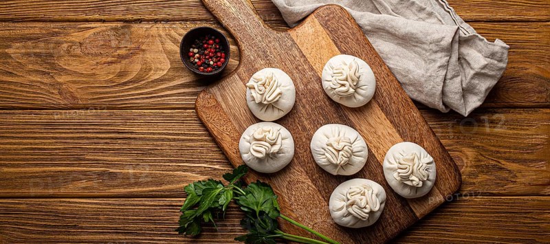 Raw freshly made Khinkali, traditional dish of Georgian Caucasian cuisine, dumplings filled with ground meat on white plate with herbs on wooden rustic background table top view space for text