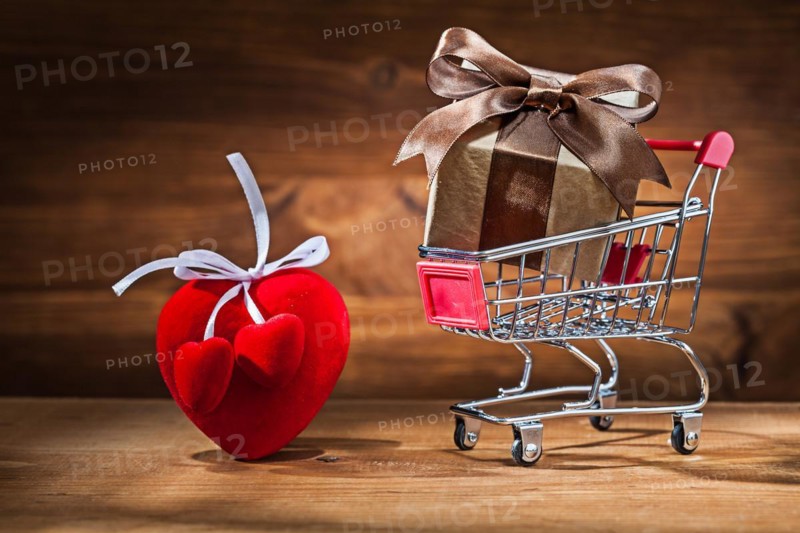 Gift box in shopping trolley and Valentine's heart toy on vintage wood