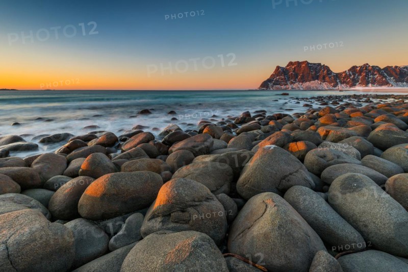 The famous beach near Uttakleiv with round shaped rock boulders on the Lofoten islands in Norway on clear winter day with snow-clad mountains and blue sky after sunset