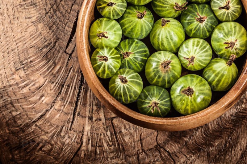 Ripe gooseberries in round bowl on vintage wooden background