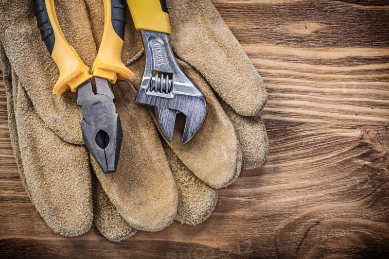 Leather safety gloves adjustable spanner pliers on wooden board construction concept