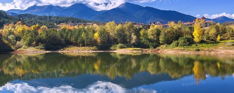 Bansko, Bulgaria autumn banner panorama background of Pirin mountain peaks, Krinets lake water, colorful green, red and yellow trees reflection