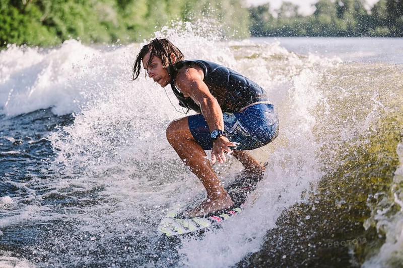 Active wakesurfer jumping on wake board down the river waves. Surfer on wave. Male athlete training on wakesurf training. Active water sports in open air on board. A man catches a wave on surf
