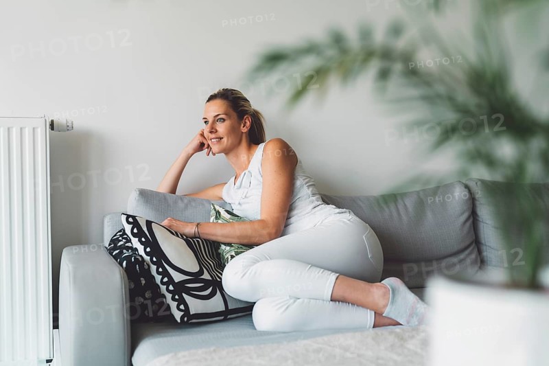 Cheerful happy caucasian woman relaxing at home on her day off work. Adult content woman spending time at home, in her apartment, resting on the couch, having a cup of coffee, feeling good
