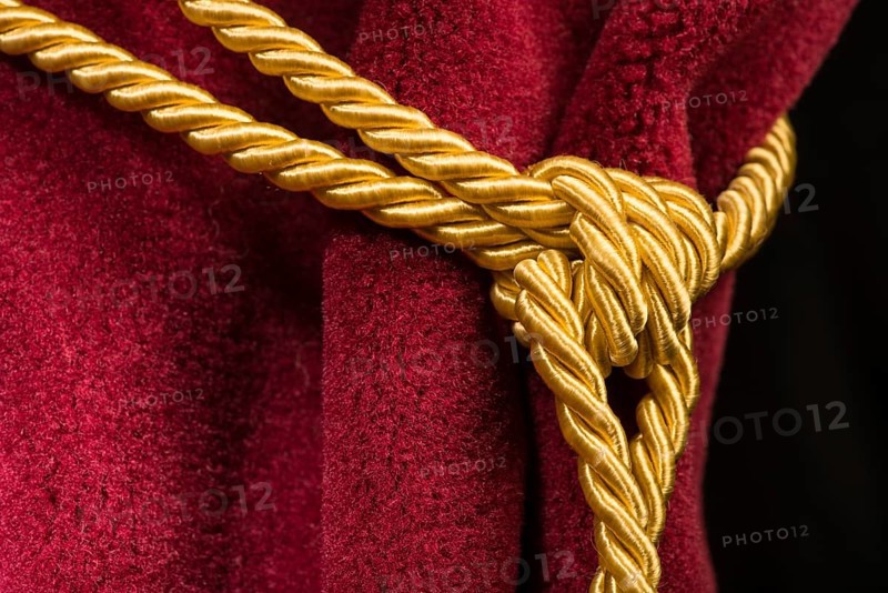 Red velvet curtain with tassel. Close up knot on rope