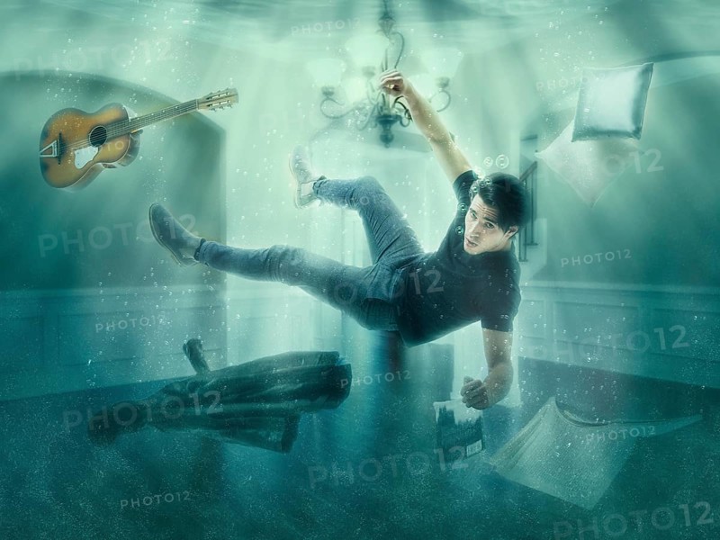 Illusion of man floating underwater among objects in room looking at camera