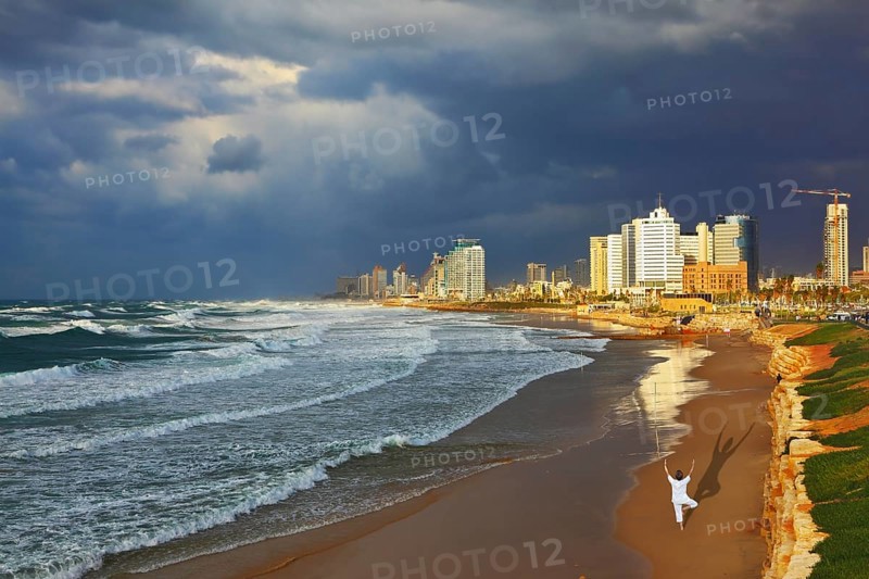 Storm cloud hanging over the sea, the woman in white performs yoga on one leg. Promenade and beach in Tel Aviv