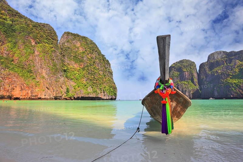 Scenic green islands of Thailand coast. Emerald sea and fine white sand. On the beach approached by a native boat for tourists, decorated with a red silk scarf