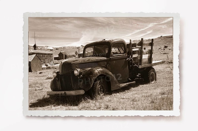 Old lorry rusting in a meadow in the former gold mining town of Bodie. Photo in sepia tone with white jagged edge in the character of old photos and a reclining shadow. Old truck is rusting on the site of the former gold mining town of Bodie. Photo in sepia tone with white jagged edge in the character of old photos