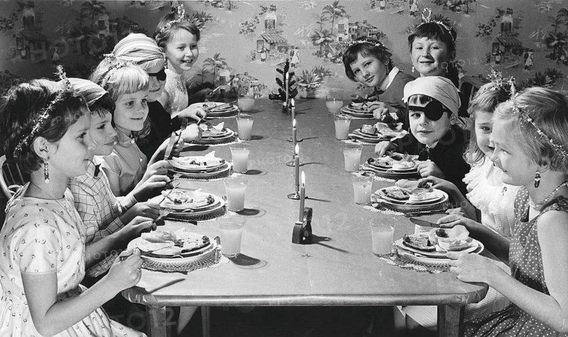 Children in the 1950s. Girls and boys dressed up in hats and costumes are sitting a table together celebrating something, eating cake and having lemonade. Sweden 1957