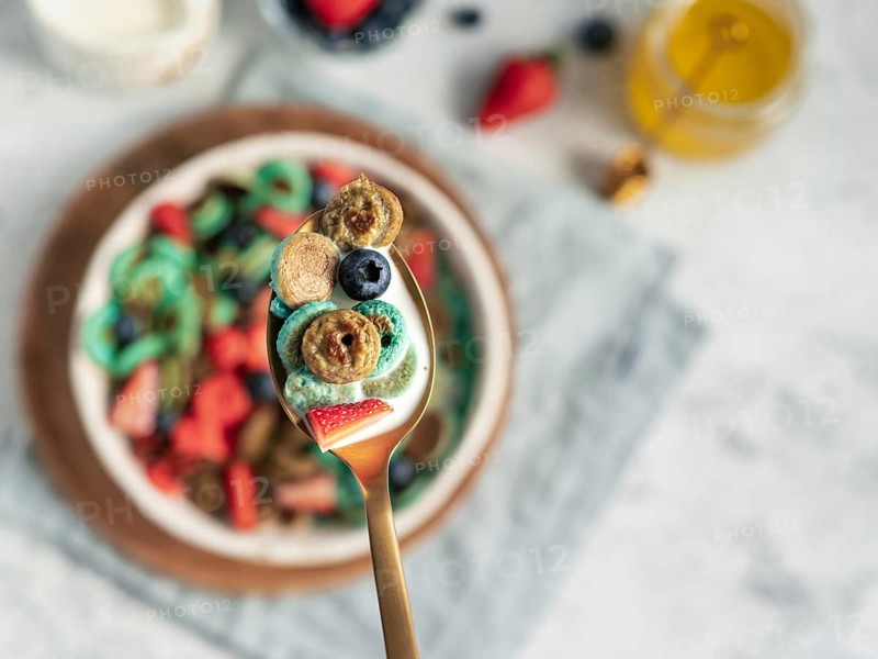Trendy food - pancake cereal. Bowl of colorful mini cereal pancakes in spoon with milk. Tiny pancakes with natural color - green matcha, turquose spirulina, blue pea, red fragon fruit. Copy space