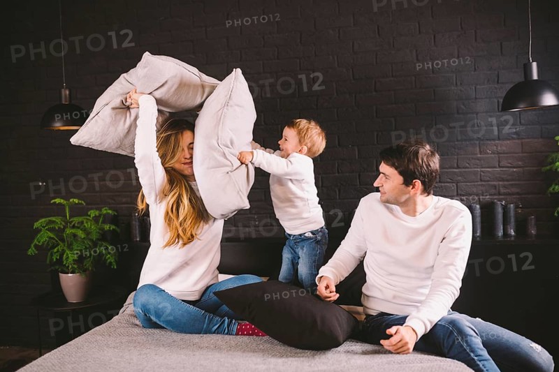 Parents with smiling child playing pillow fight on bed, happy family having fun in bedroom, enjoying leisure activity, funny weekend lifestyle. Happy family having fun in bedroom, pillow battle