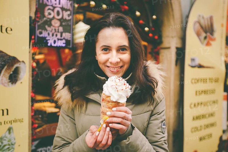 A beautiful girl in a warm jacket eats trdelnik or Trdlo with cream in her hands, in the winter in the Czech Republic, Prague at the Christmas market