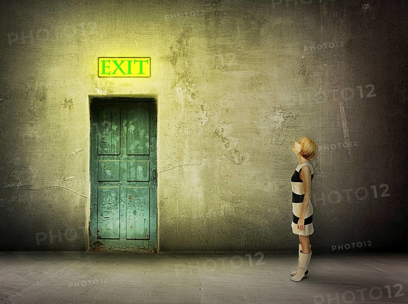 Young woman in black and white dress stand in front of blue door in dark grungy room watch on glowing exit sign, find the way out