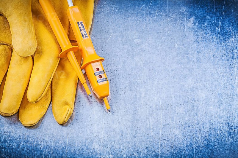 Yellow electrical tester safety gloves on metallic background electricity concept