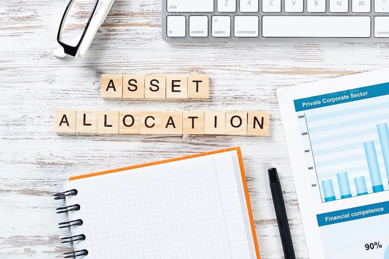 Asset allocation concept with letters on cubes. Still life of workplace with supplies. Flat lay vintage white wooden desk with computer keyboard and spiral notebook. Capital investment and management