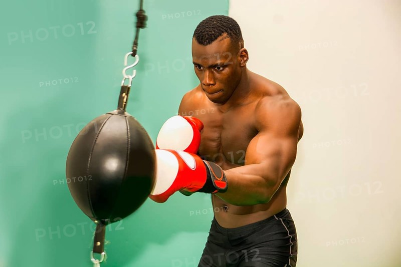 African male boxer punching ball wearing boxing gloves, back profile view