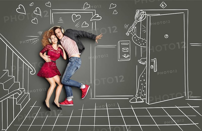 Happy valentines love story concept of a romantic couple sharing headphones and listening to the music on the stairs too loud for the neighbours, against chalk drawings background