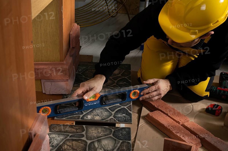 While laying the terracotta, the general construction worker checks the correctness of execution with a spirit level. An employee wearing personal protective equipment