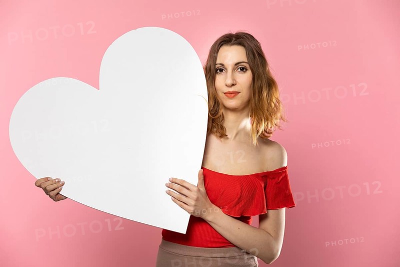 A beautiful girl in love holds a heart shape in her hand. Young woman wants to give a beautiful heart shape as a symbol of love on Valentine's Day