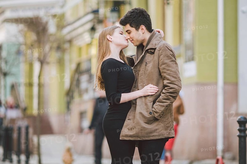Urban modern young love couple walking romantic talking talking, holding hands on a date. Young multicultural Turkish brunette and Caucasian couple on old european street. Autumn spring weather