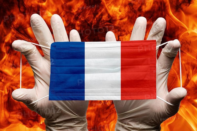 Doctor holding in white gloves protection medical face mask, respiratory bandage with France national country flag superimposed on mask. Concept on background of dangerous red flames natural fire