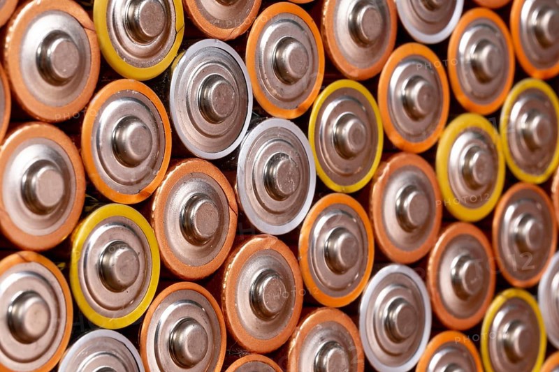 Multiple used AA alkaline batteries are seen arranged in a pile. Closeup side view from the plus side of the battery