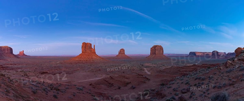 A panorama picture of the Monument Valley landscape in the early evening or night, with the West Mitten Butte, East Mitten Butte and Merrick Butte rock formations in the center