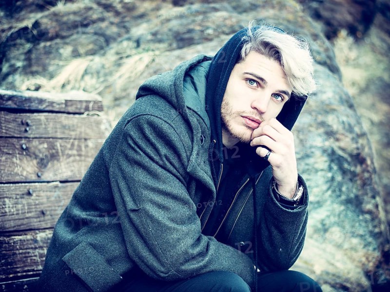 Portrait of young man in hoodie posing outdoor in winter setting with snow all around, looking at camera