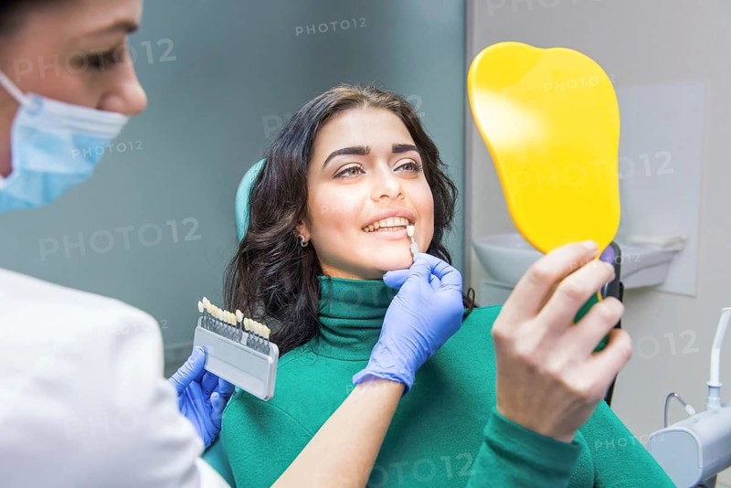 Female dentist, patient holding mirror. Tooth shade chart