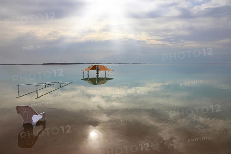 Medical beach on the Dead Sea, Israel. Round gazebo and a beach chair in the water. Cloudy sky reflected in water