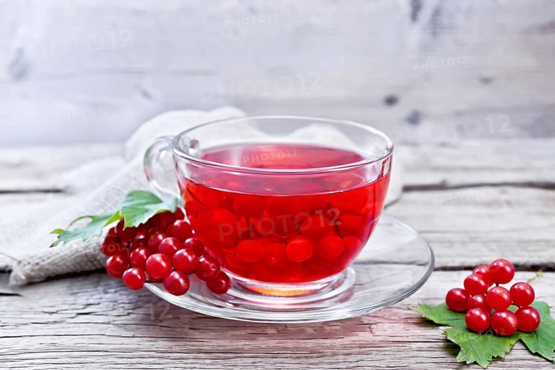 Tea with viburnum in a glass cup, berries and green leaves, burlap on wooden board background