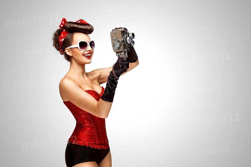 Retro photo of a pin up girl with an old 8 mm camera on a grey background