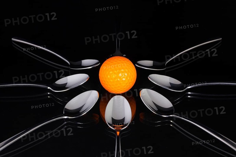 Teaspoons and orange golf ball on the black glass table