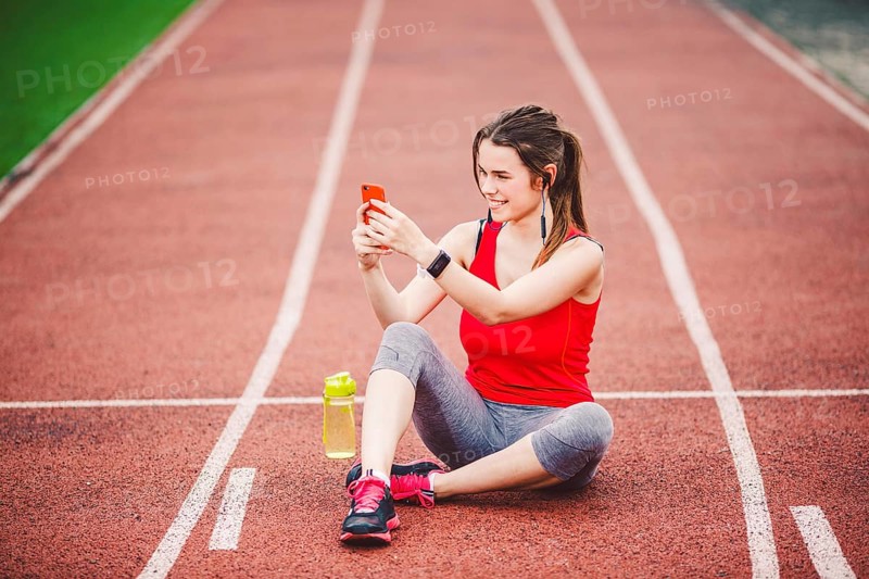 Beautiful fitneß girl uses smartphone at stadium after workout. Sports and healthy. Sport woman use of cellphone inside sport complex. Sport and technology. resting after workout, run at red track