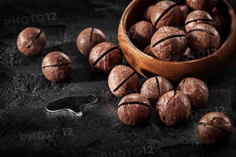 Macadamia Nuts And Key For Open It With Wooden Bowl On Black Background