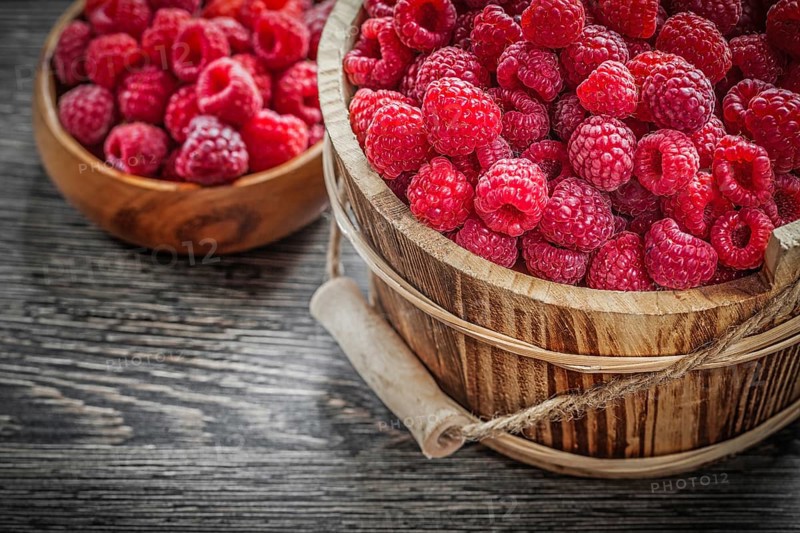 Bowl and bucket with raspberries on wooden board