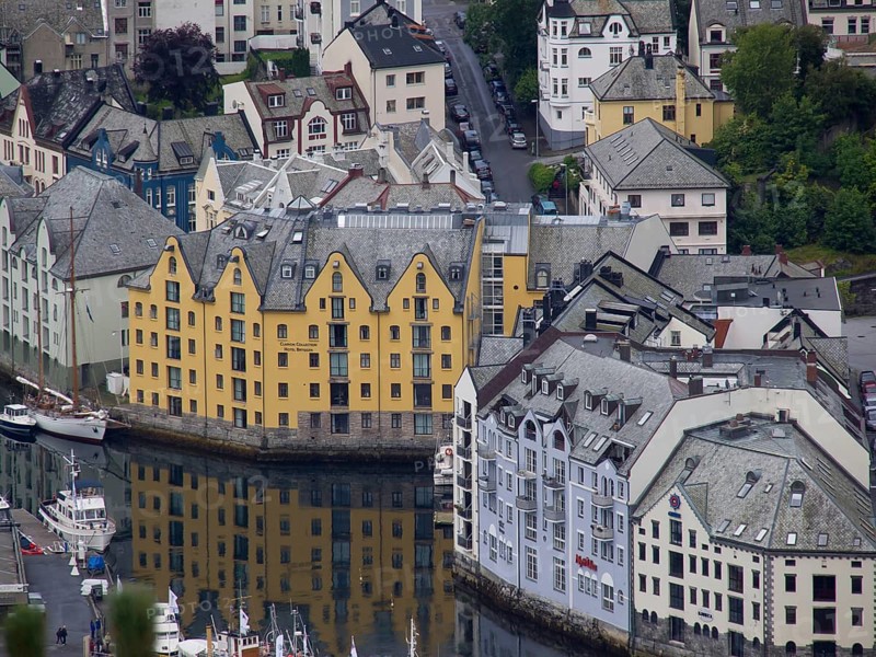 Yellow and white houses are reflected in the canal, surrounded by several small boats, alesund, norway