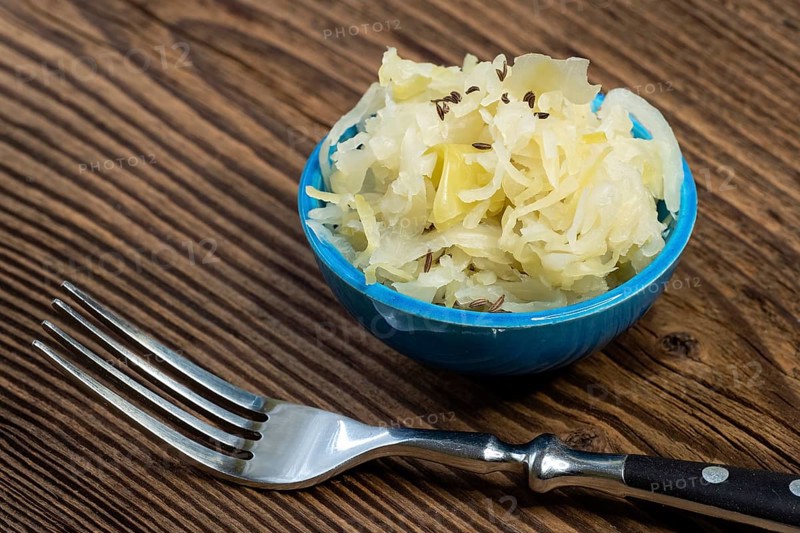 Homemade pickled sauerkraut in a bowl with a fork on a wooden board
