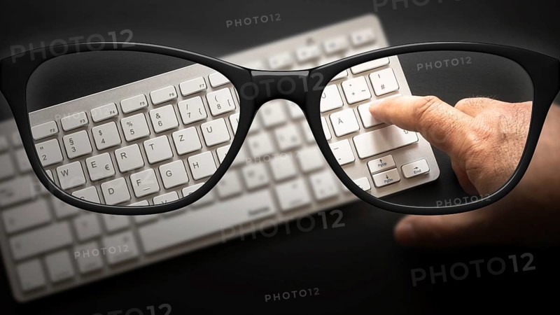 Some black glasses with keyboard sharp and blurred