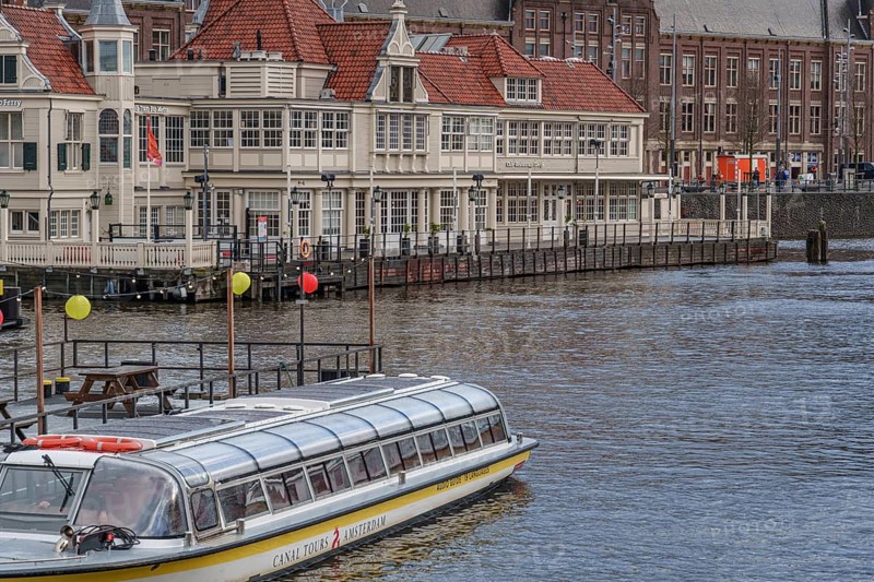 Houseboat in front of a historic building with red roofs on the canal, Amsterdam, Netherlands