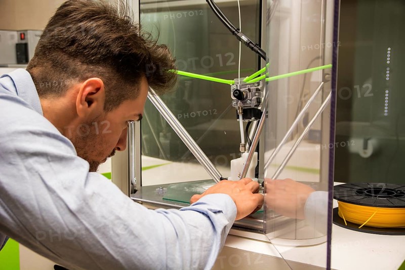 Brunet adult man working with 3D printer, observing the machine at work